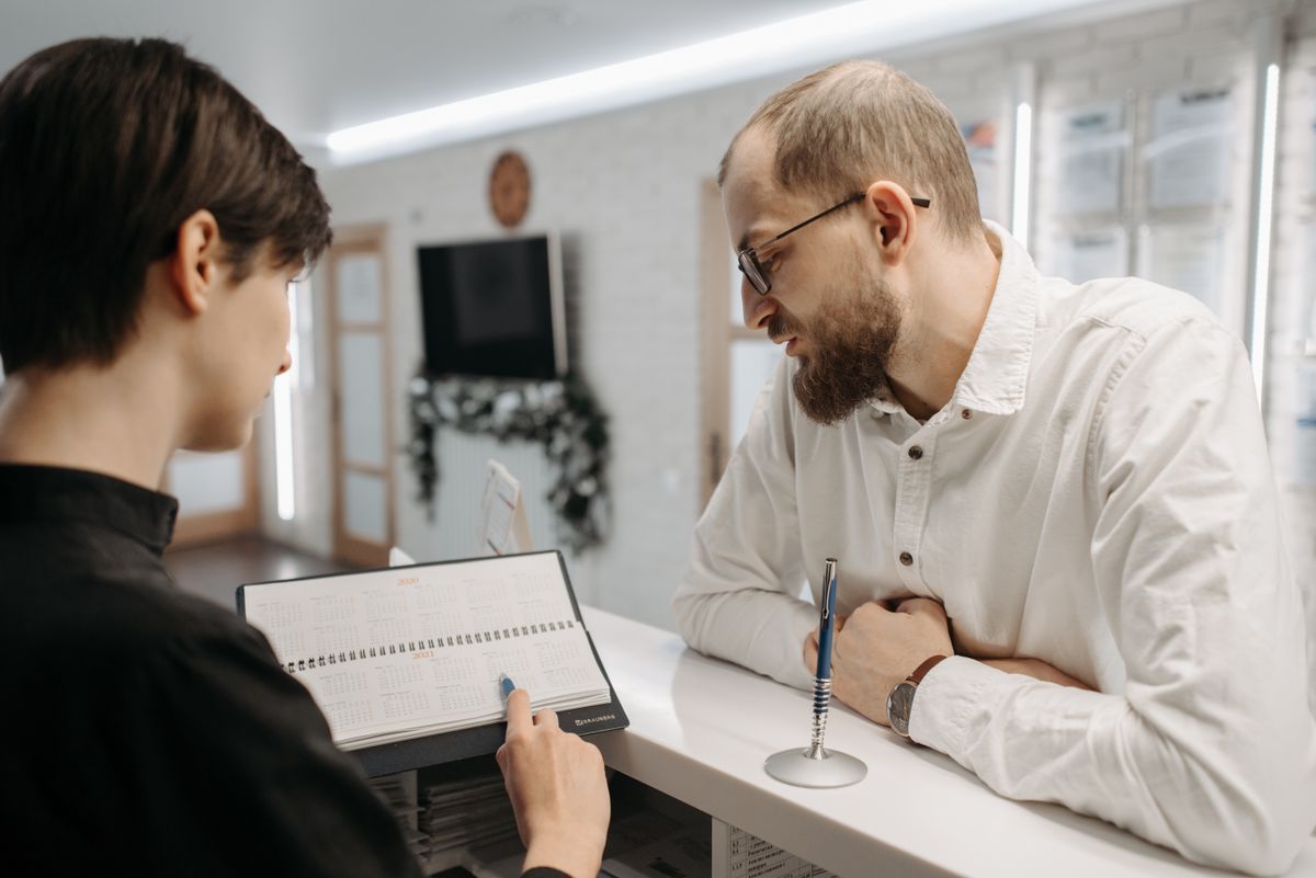 A clinic front desk where a staff member reviews a checklist with a visitor