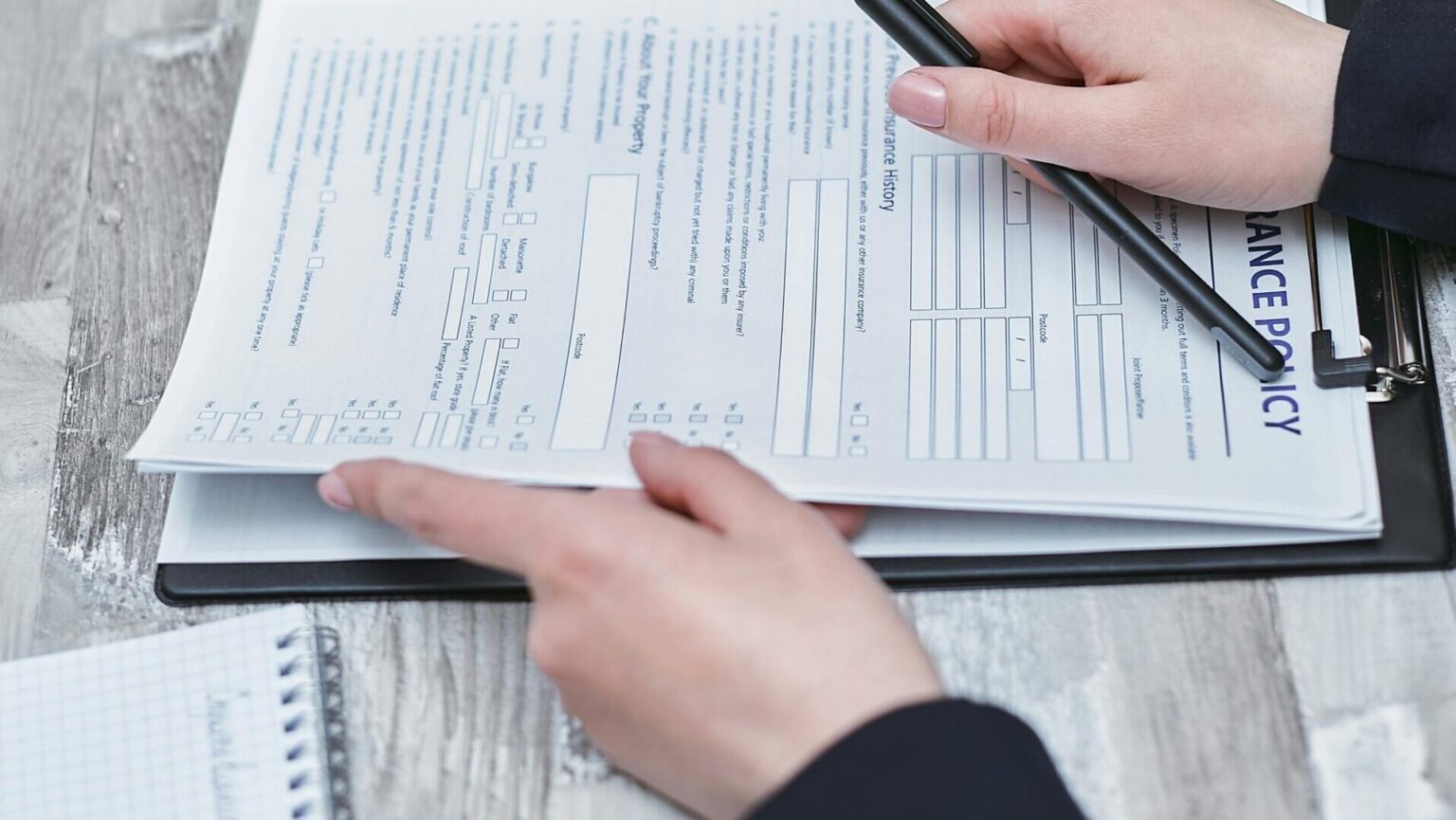 Hands filling in a printed insurance questionnaire on a clipboard